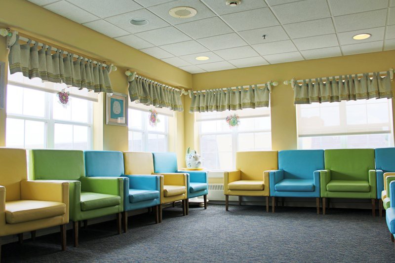A colorful waiting room in a hospital with blue, green, and yellow chairs arranged around the space.