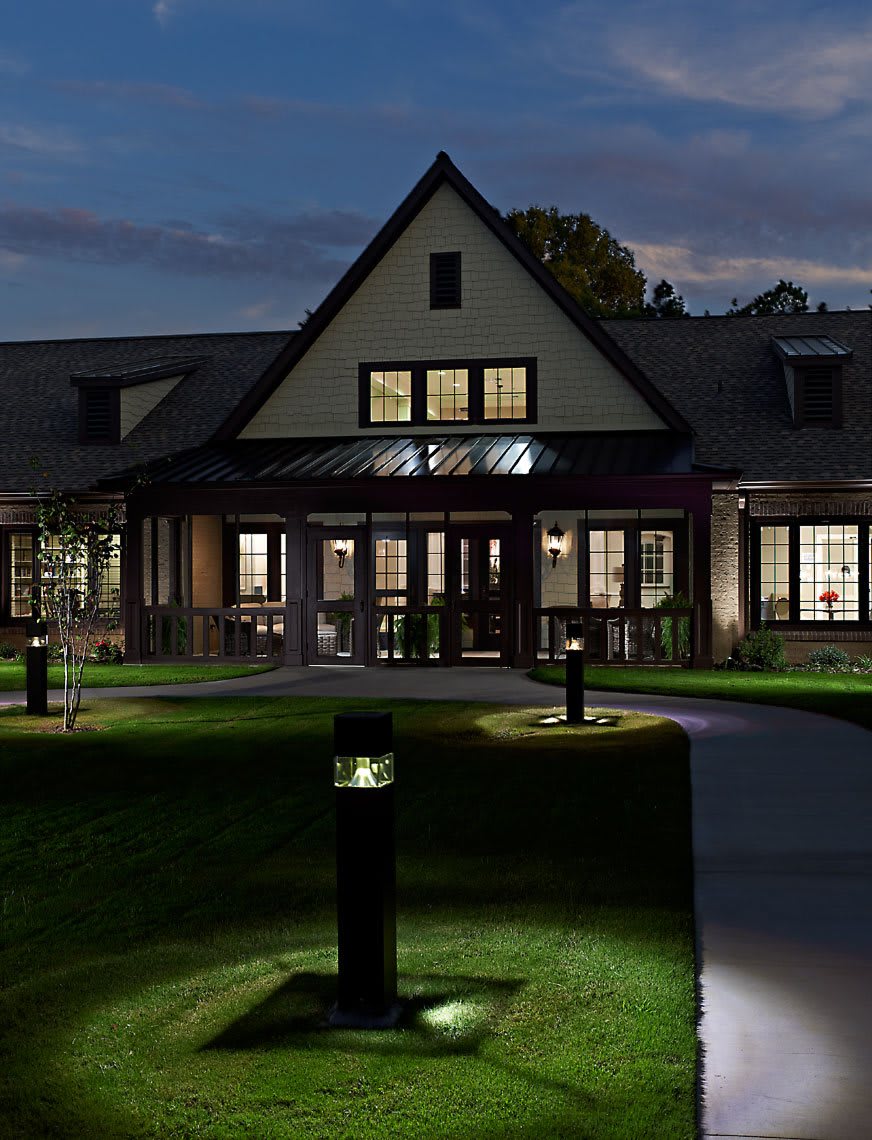 A well-lit building at night with a lawn and pathway leading to the entrance.