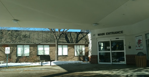 A view of the entrance to a building, featuring large windows and trees in the background.