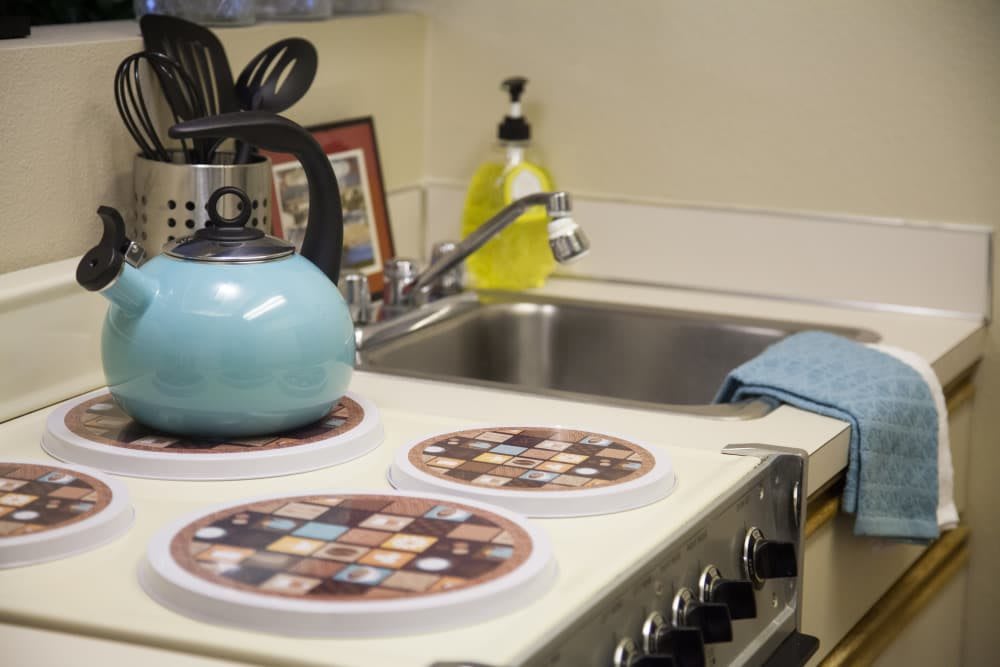 A cozy kitchen corner with a blue teapot on the stovetop and utensils by the sink.