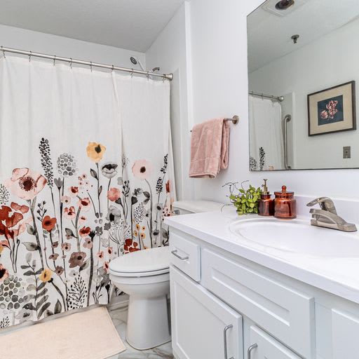 A clean and bright bathroom with a floral shower curtain and white cabinetry.