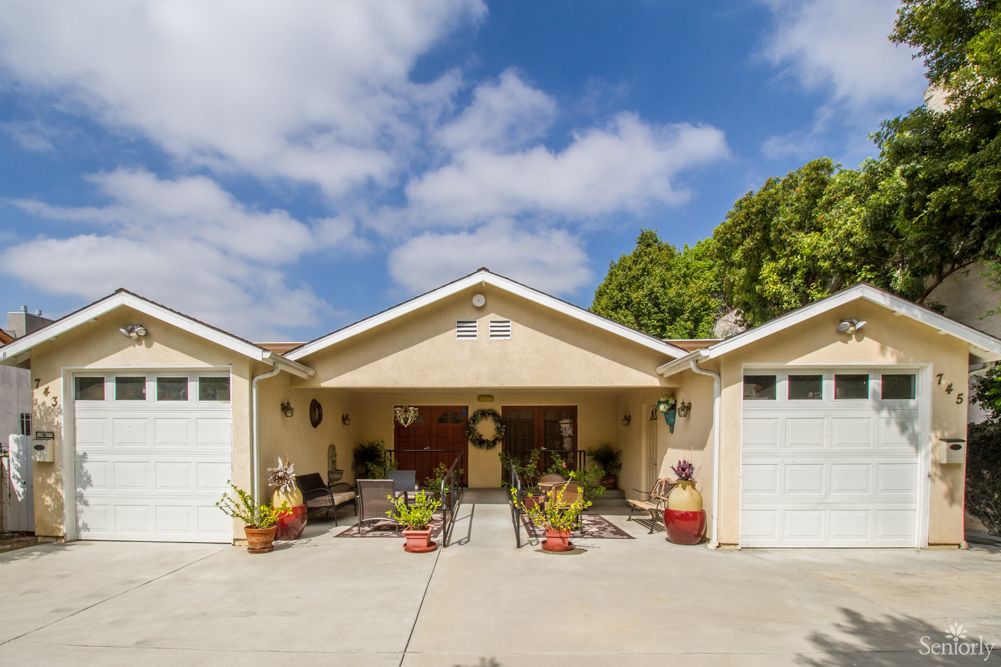 A suburban house with a driveway and two garages, surrounded by greenery.