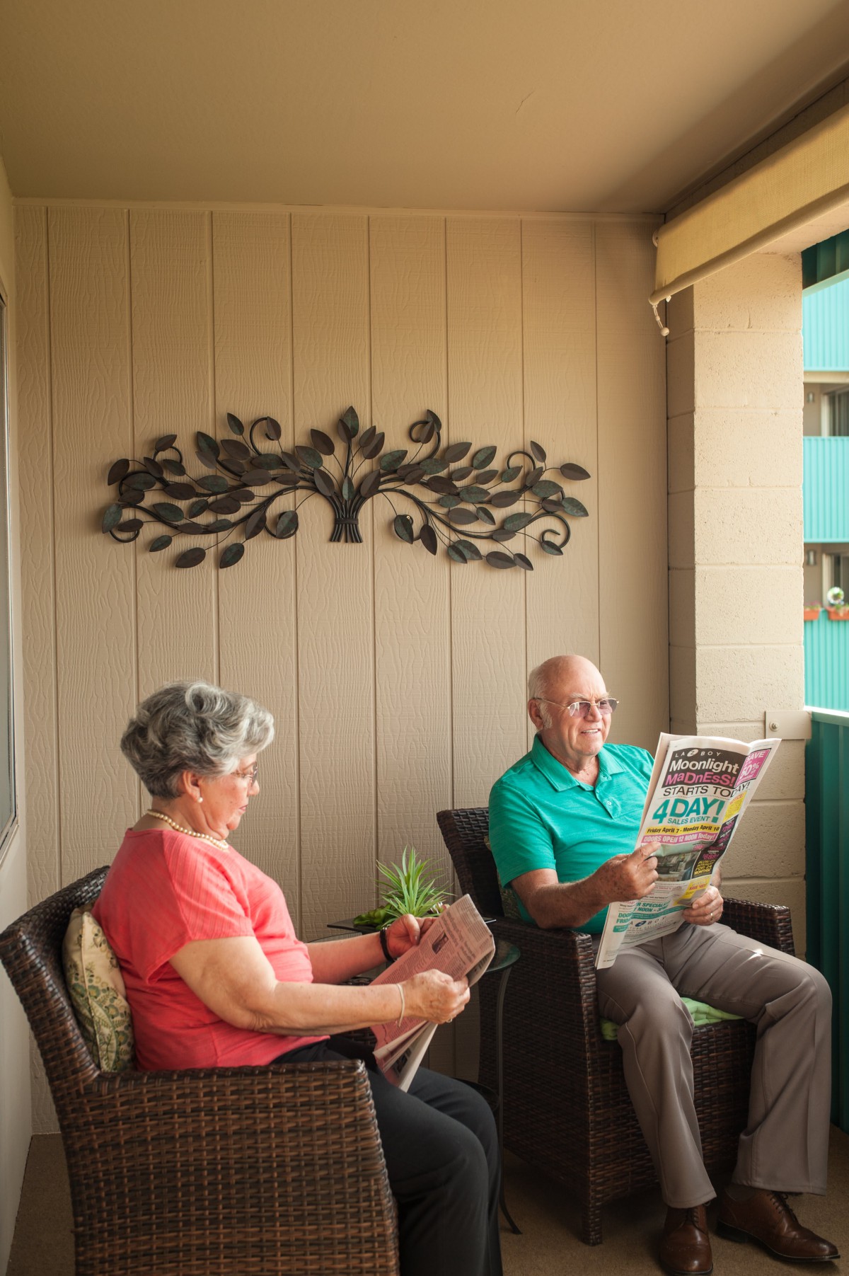 An elderly couple relaxing on a balcony, reading a book and a newspaper.