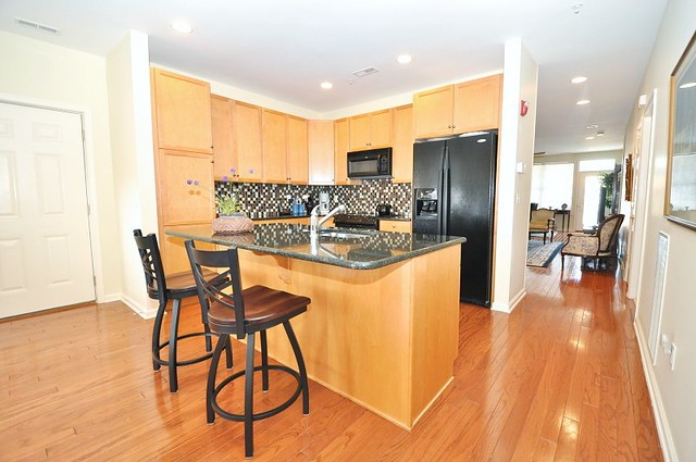 A modern kitchen featuring an island with bar stools, wooden cabinets, black appliances, and a granite countertop.