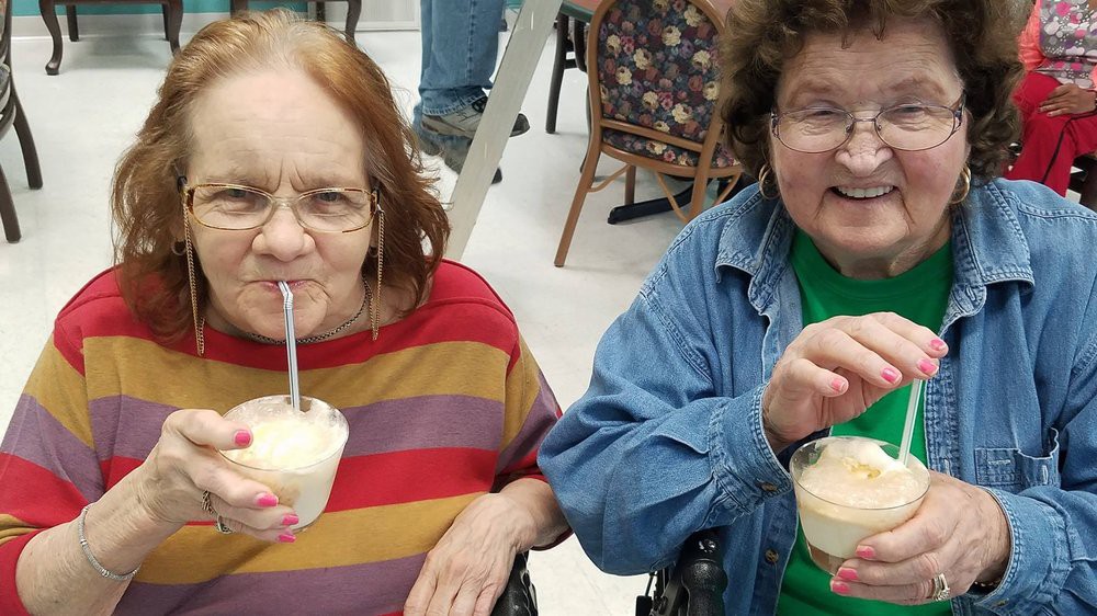 Two elderly women enjoy ice cream indoors, smiling and relaxed.
