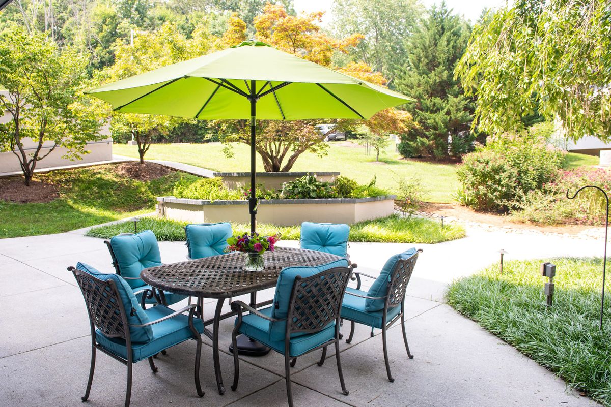 A cozy patio setup with a table, umbrella, and chairs in a lush backyard setting.