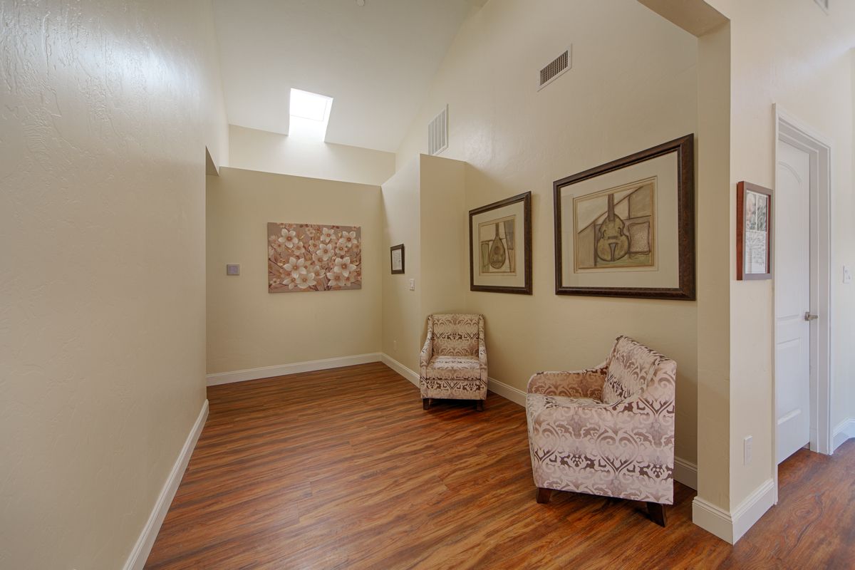 A cozy hallway with two patterned chairs and artwork, featuring a wooden floor and skylight.