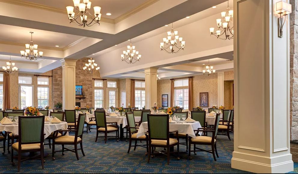 An elegant dining room with neatly arranged tables and chairs, illuminated by decorative chandeliers.