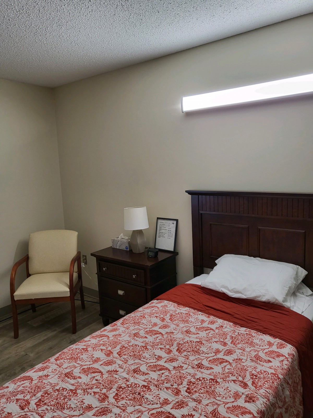 A simple bedroom with a single bed, nightstand, and chair.