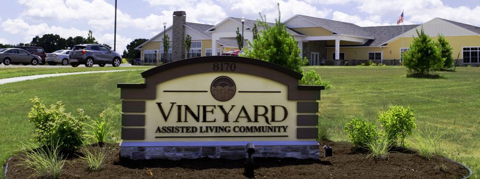 Entrance sign for Vineyard Assisted Living Community with buildings in the background.