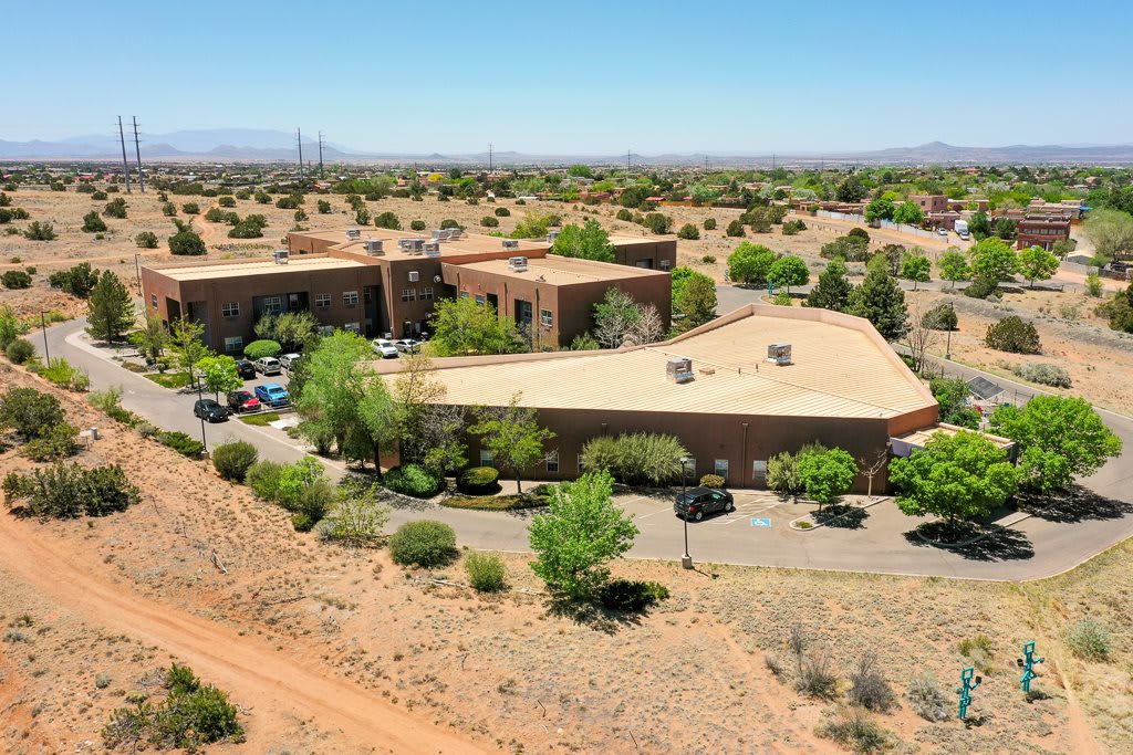 Aerial view of a building complex surrounded by desert landscape and greenery under a clear blue sky.
