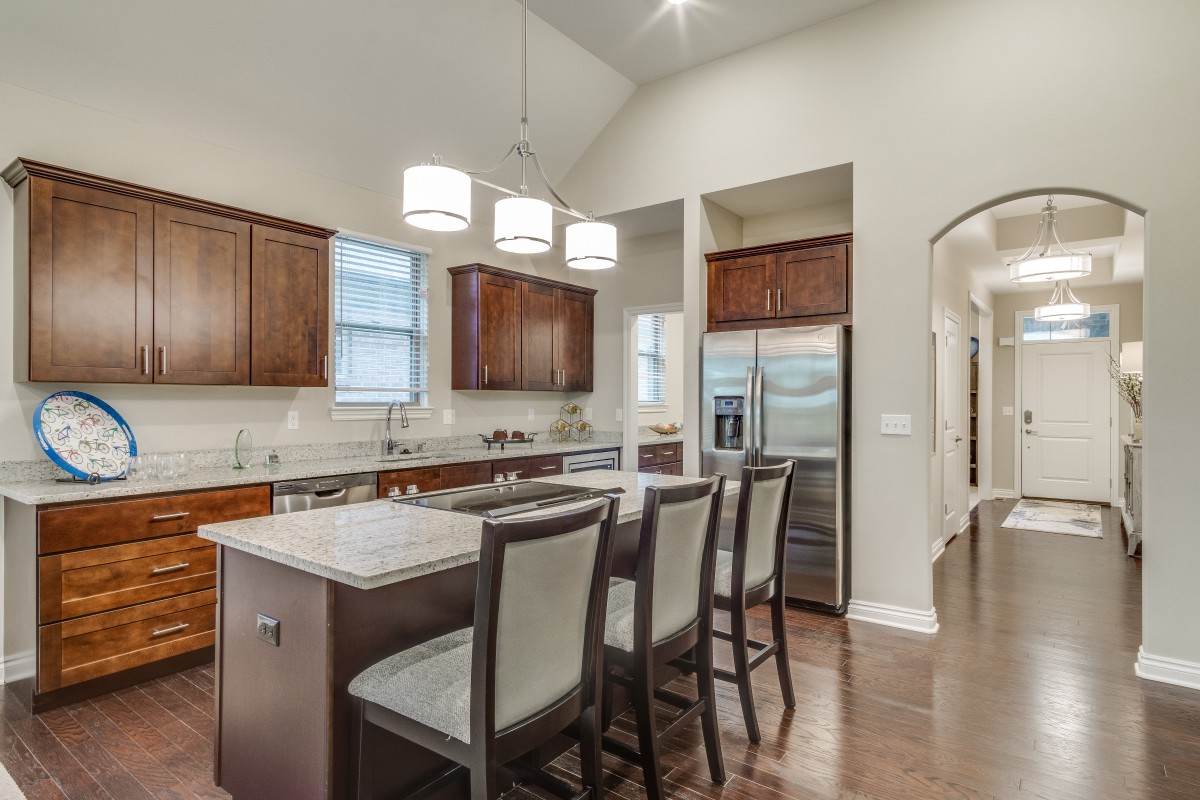 A modern kitchen with a central island and bar stools, featuring wooden cabinets and stainless steel appliances.