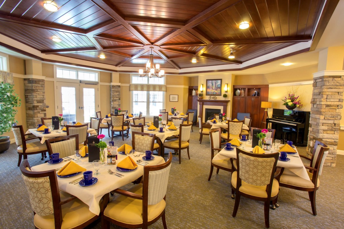 An elegantly decorated dining room with neatly arranged tables and chairs, featuring a wooden ceiling and chandeliers.