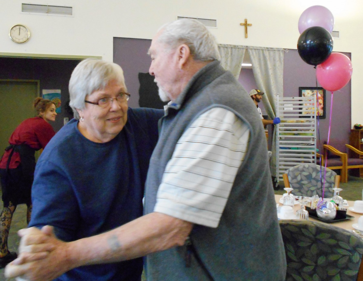 An elderly couple joyfully dancing at an indoor celebration with balloons.