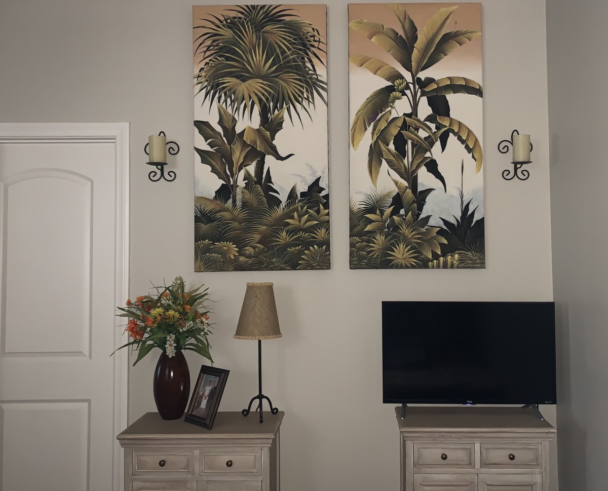 A cozy living room corner featuring tropical wall art, a small television, and a dresser adorned with a lamp and floral arrangement.