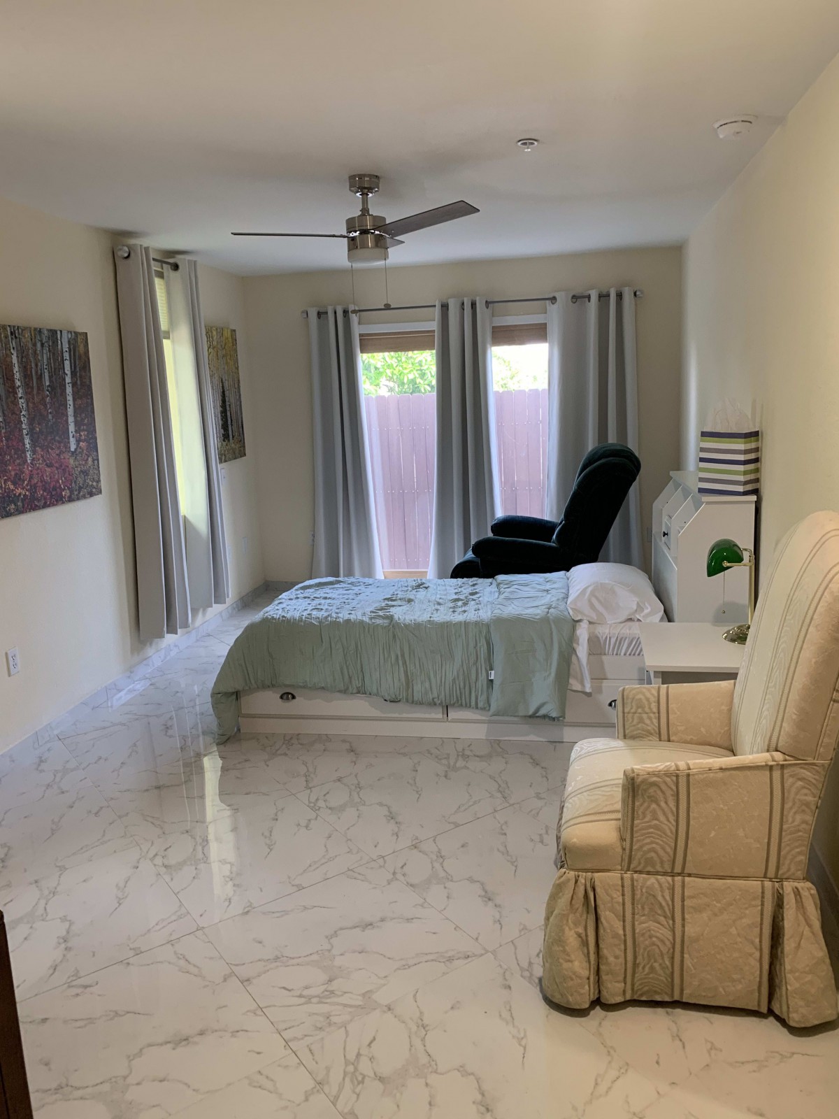 A bright and cozy bedroom with a bed, armchair, and large windows with curtains.