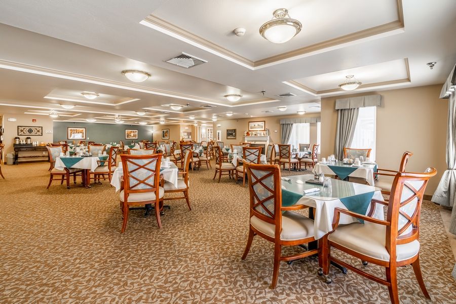 An elegant dining room with neatly arranged tables and chairs, featuring stylish lighting and a carpeted floor.