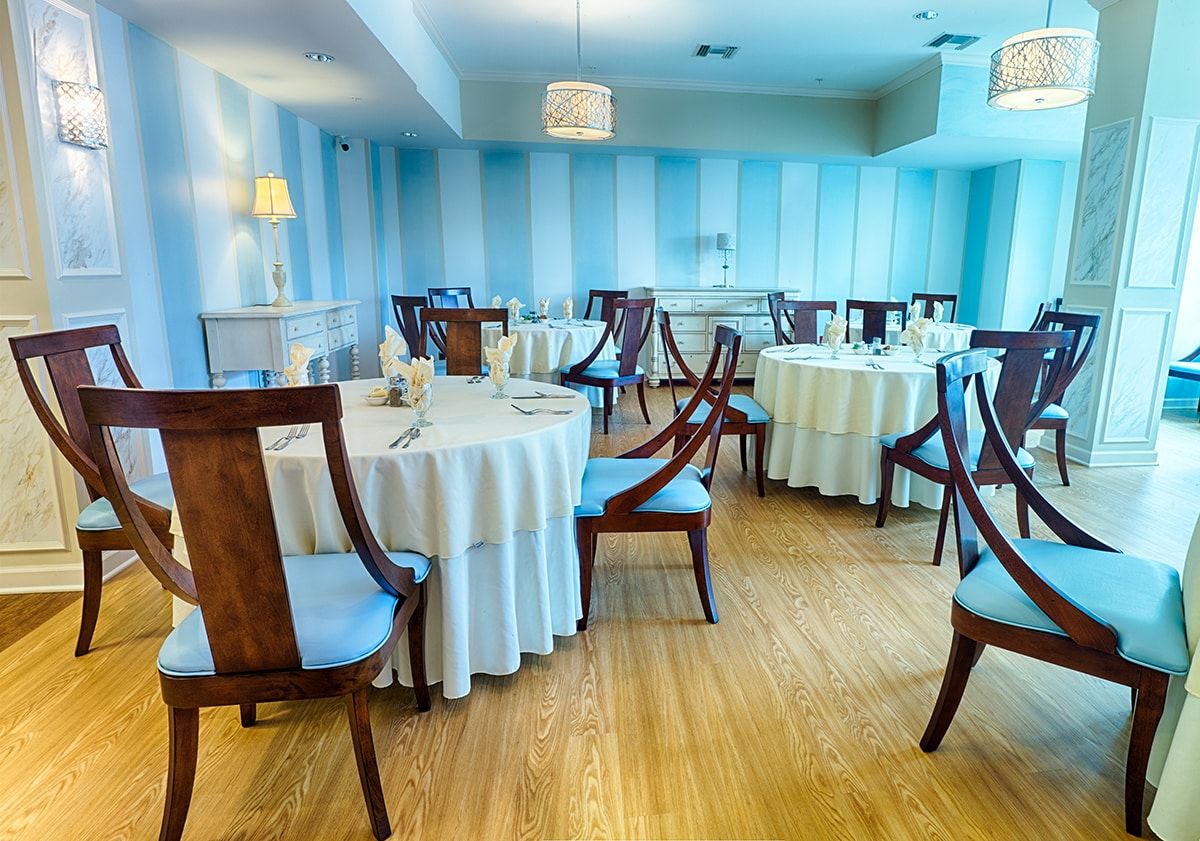 An elegant dining room with round tables set for guests, featuring blue walls and wooden floors.