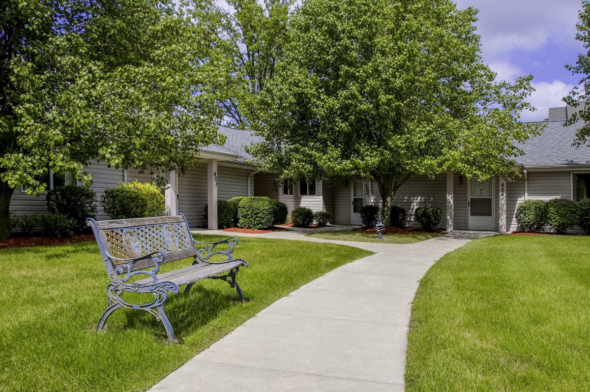 A serene garden path leading to a house, flanked by trees and a bench.