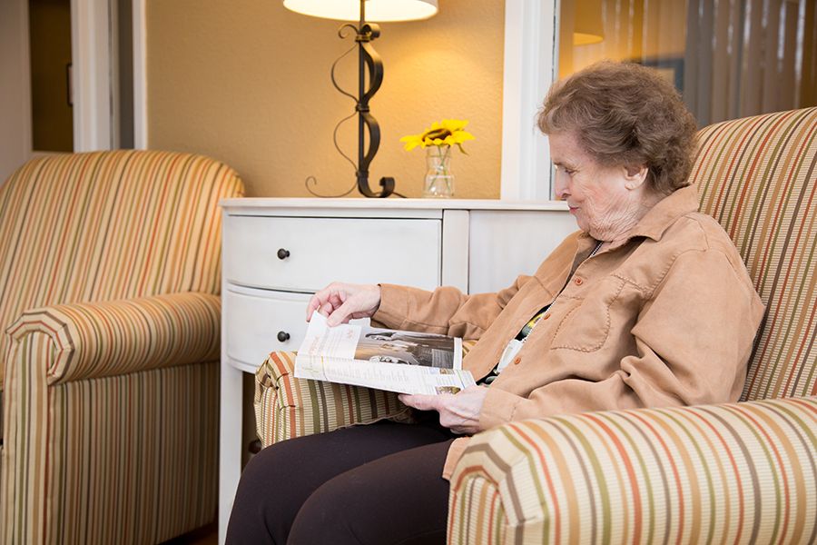 An elderly woman sitting in a comfortable chair, reading a book in a cozy living room setting.