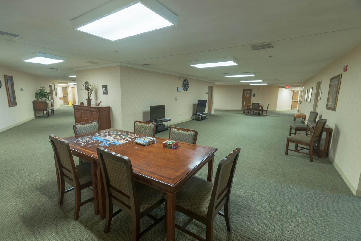 An office space with a meeting table surrounded by chairs, featuring television sets and ample lighting.