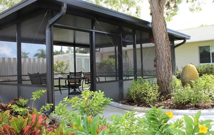 A screened porch with outdoor seating surrounded by a garden.