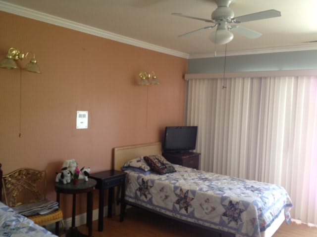 A cozy bedroom featuring two beds, a television on a stand, and a ceiling fan.