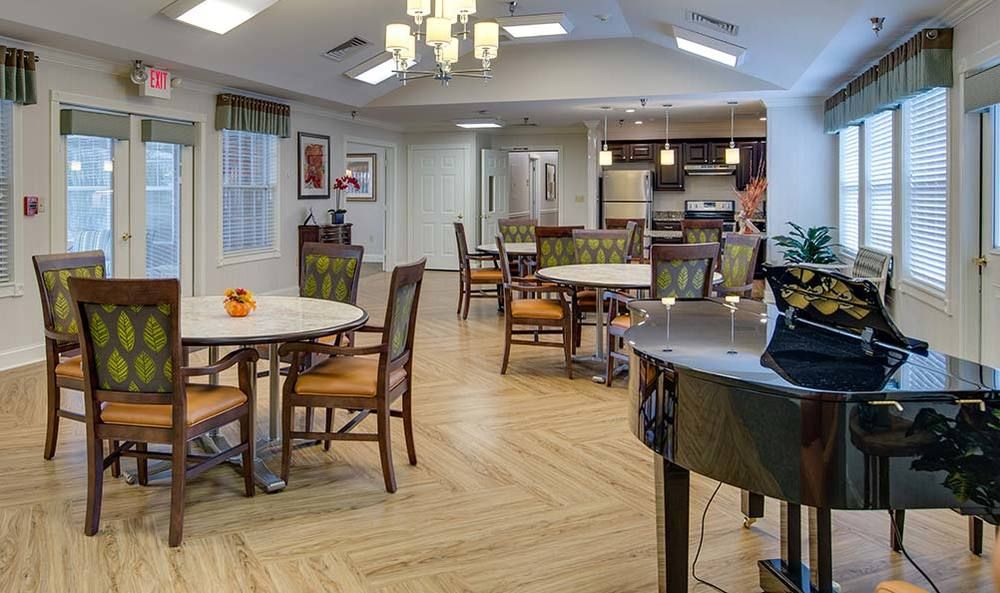 A modern dining area with wooden tables and chairs, featuring an open kitchen and elegant lighting.