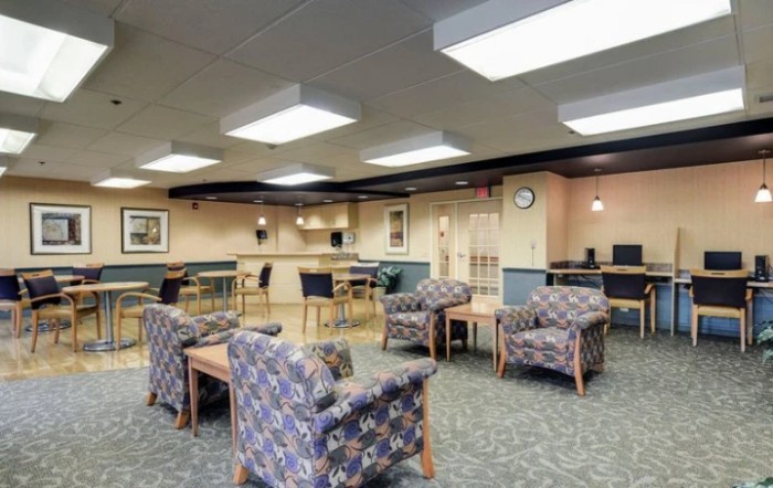 A spacious waiting room with patterned chairs and tables, featuring bright overhead lighting.