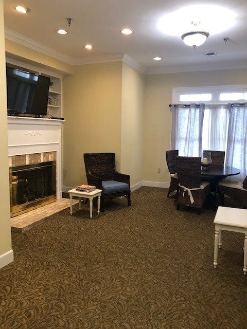 A cozy living room with a fireplace and television, featuring comfortable chairs and a dining table.