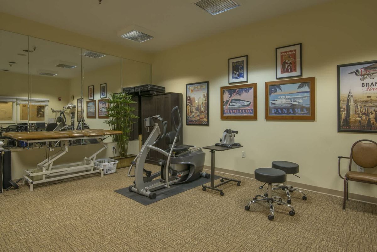 A well-equipped exercise room featuring fitness machines, wall mirrors, artwork, and comfortable seating.