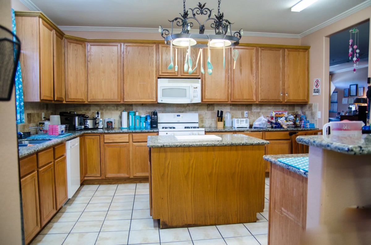 A spacious kitchen with wooden cabinets, a central island, and a decorative chandelier.