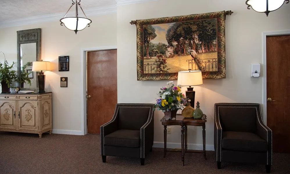 A cozy waiting room with two chairs, a decorative lamp on a table, and artwork on the wall.