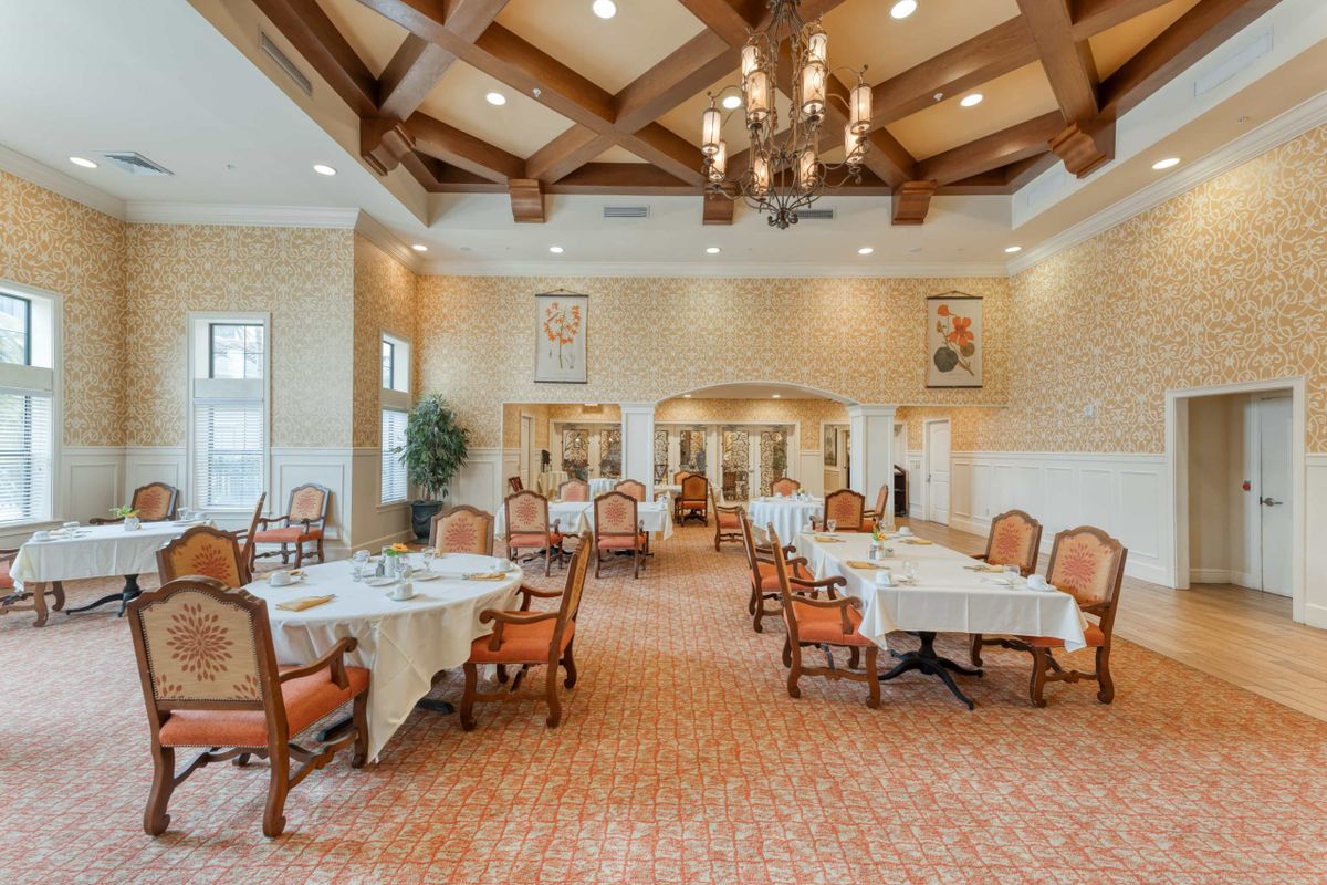 A spacious and elegantly decorated dining room with tables and chairs arranged neatly under a chandelier.