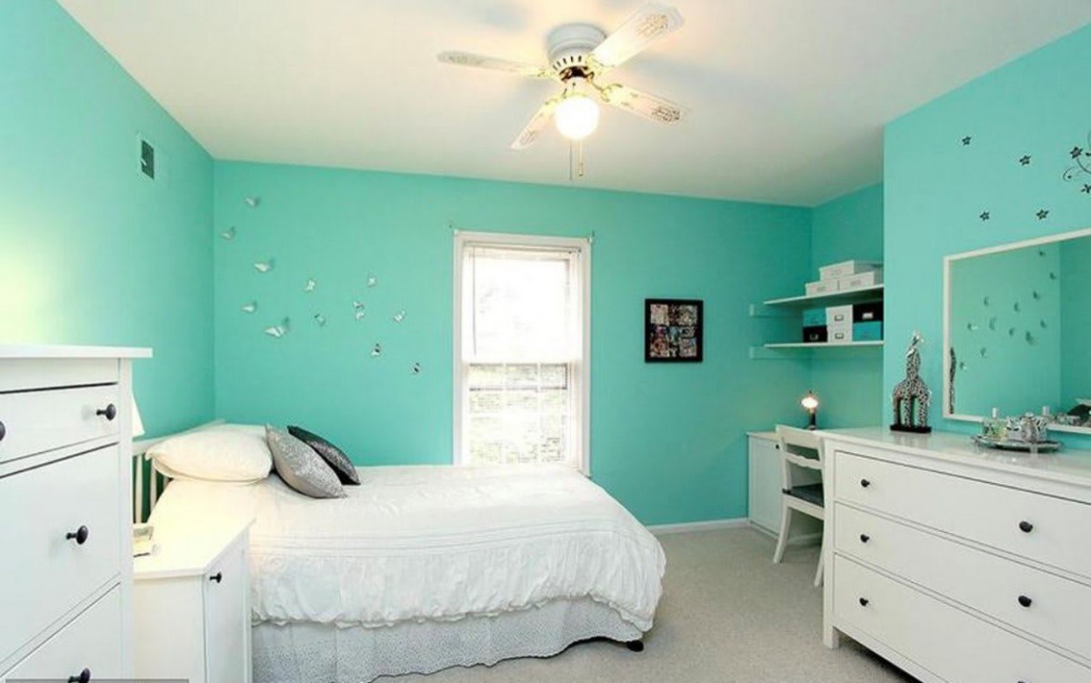 A cozy bedroom with turquoise walls, featuring a single bed, desk, and shelves.