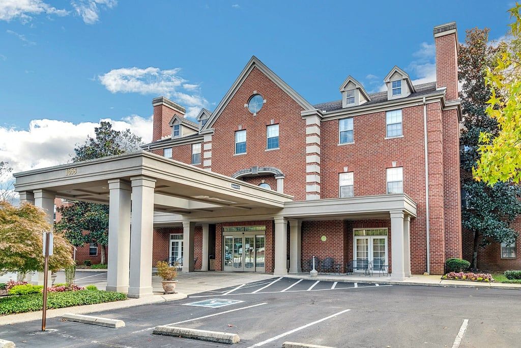 A brick facade hotel building with a covered entrance and parking spaces in front.