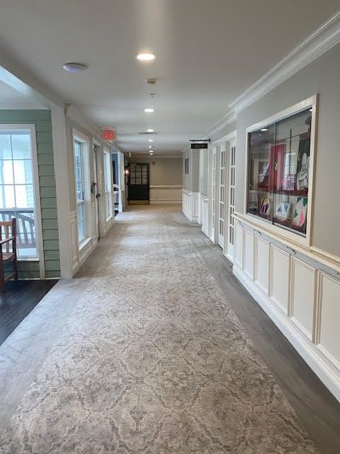 A carpeted hallway with paintings and windows on the side.