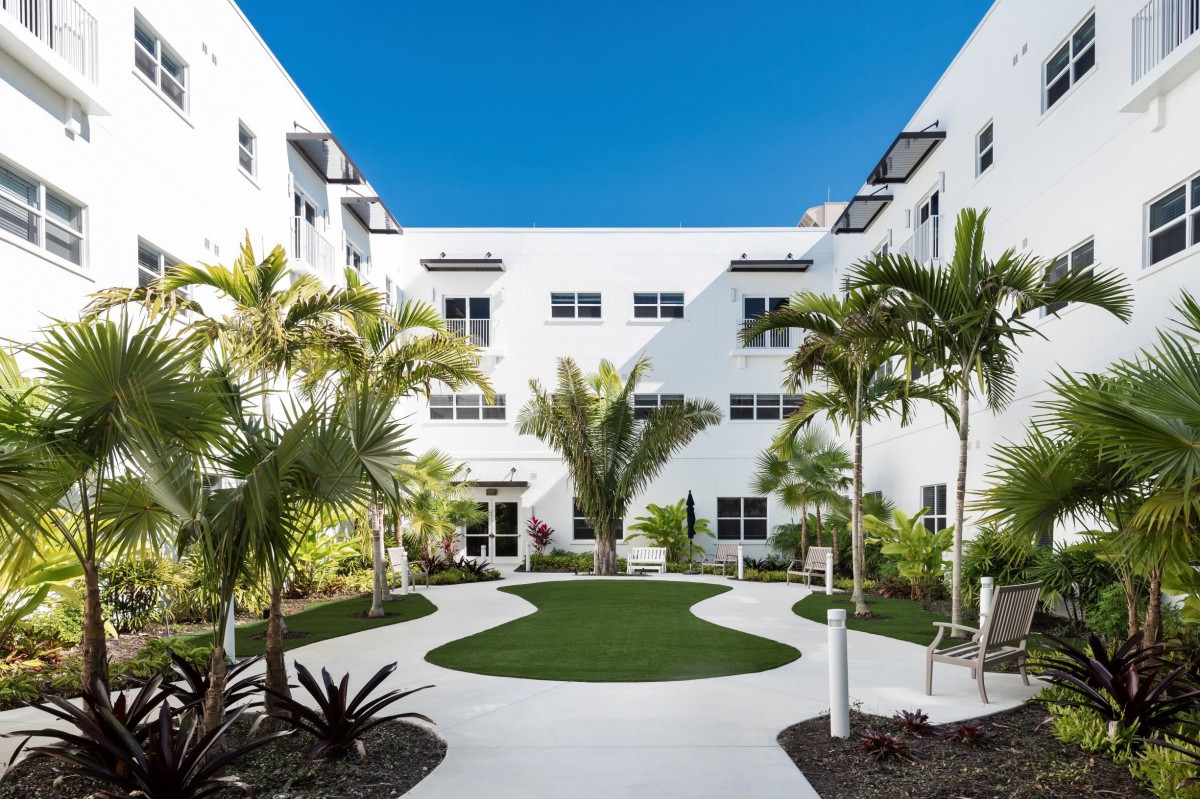 A modern courtyard with palm trees and a white building under a clear blue sky.