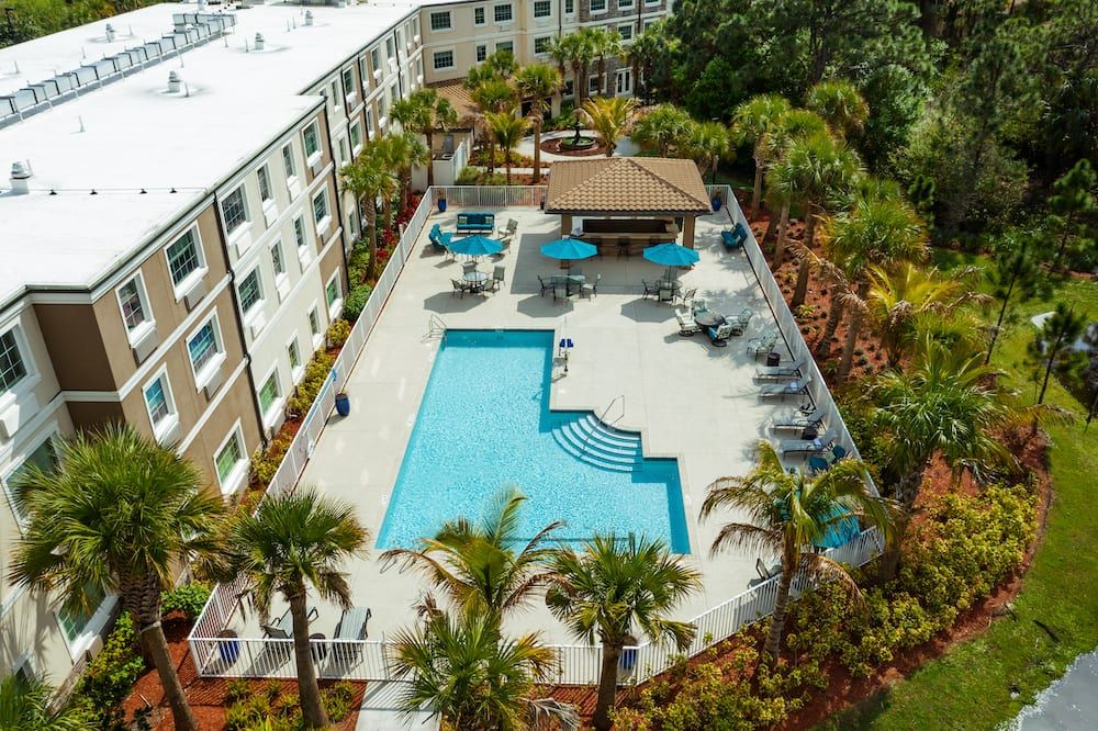 Aerial view of a resort-style swimming pool surrounded by an apartment complex and lush palm trees.