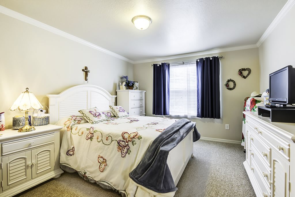 A cozy bedroom with a neatly made bed, decorated with butterfly-themed bedding and surrounded by simple furnishings.