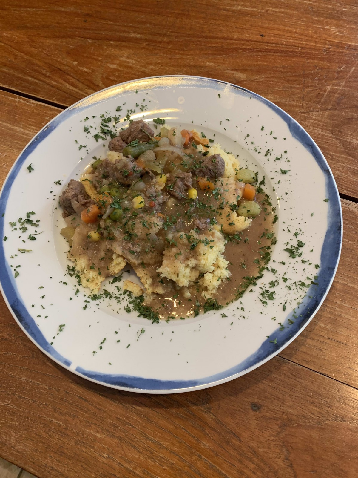 A plate of beef stew served over mashed potatoes, garnished with herbs.