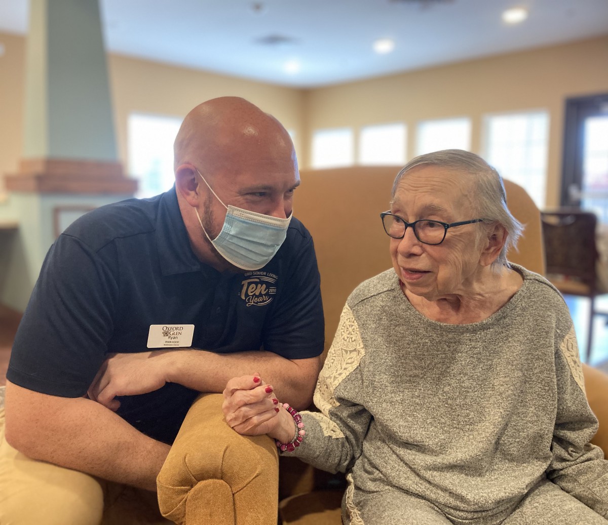 A healthcare worker in a mask conversing with an elderly person in a nursing home.