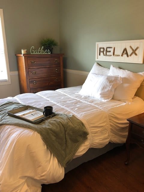 A cozy bedroom with a neatly made bed, a wooden dresser, and a 'RELAX' sign on the wall.
