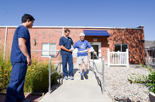 Healthcare professionals assist an elderly individual as they navigate a ramp outside.