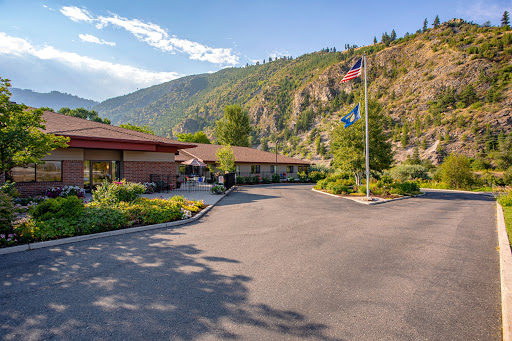 A picturesque view of a building set against a mountainous backdrop, featuring flags and lush greenery.
