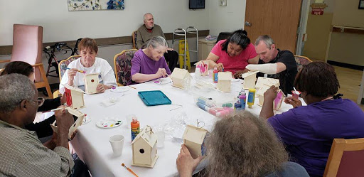 A group of individuals engaged in a creative painting activity, decorating small birdhouses at a community center.