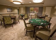 A cozy poker room with several green felt gaming tables and comfortable seating.