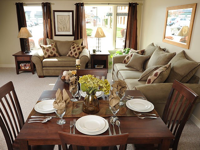 A cozy living room with a dining table set for four, featuring comfortable sofas and warm decor.