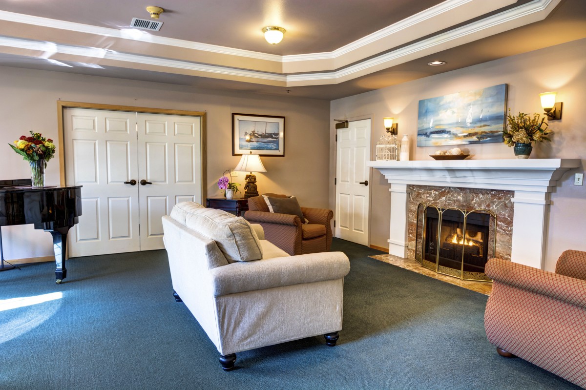 A cozy living room with a sofa, armchair, and a lit fireplace, complemented by framed artwork and warm lighting.