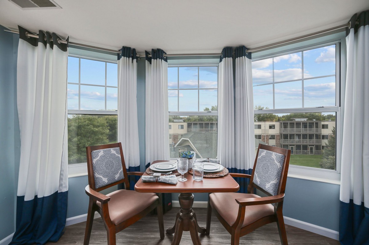 A cozy dining area with a small table set for two, surrounded by large windows allowing natural light to fill the space.
